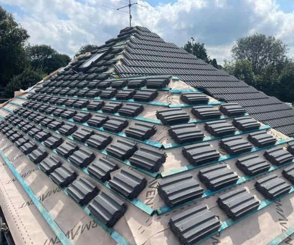 This is a photo of a new hip roof being installed. New felt, battens, and grey tiles have been installed, also a new velux window. Works carried out by PER Roofing Godmanchester