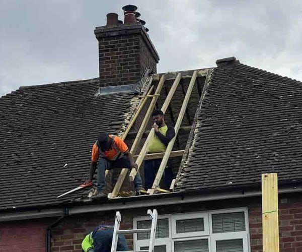 This is a photo of a roof repair being carried out. A section of the roof has been stripped and two roofers are replacing the rafters. Works being carried out by PER Roofing Godmanchester